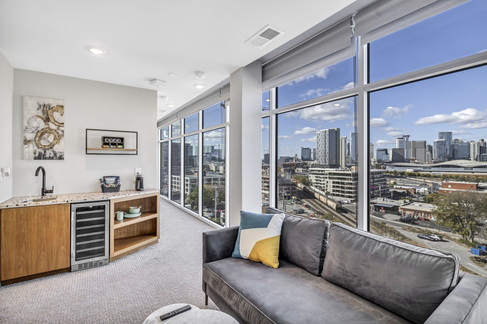 Furnished living area at Haven at The Gulch, sofa and kitchenette against a wall of windows over the Nashville skyline