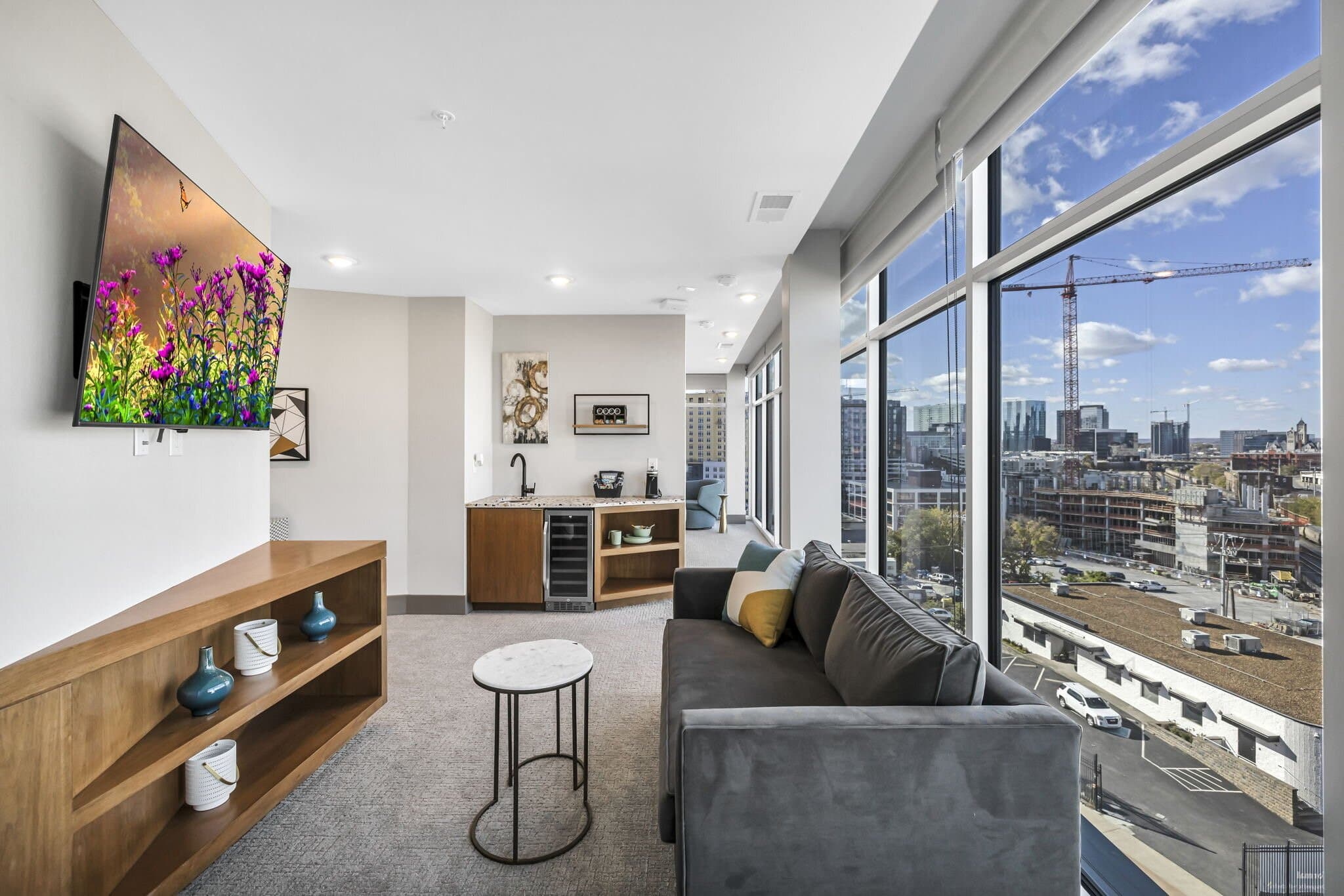 Living area with a wall-mounted television, sofa, and city views through floor-to-ceiling glass